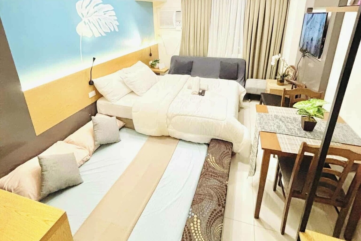 A hotel room with a bed, bedside table, lamp, curtains, and a desk with a chair.