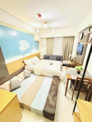 A hotel room with a bed, bedside table, lamp, curtains, and a desk with a chair. - MR BED-Skyline View Condo With POOL (Cebu City)
