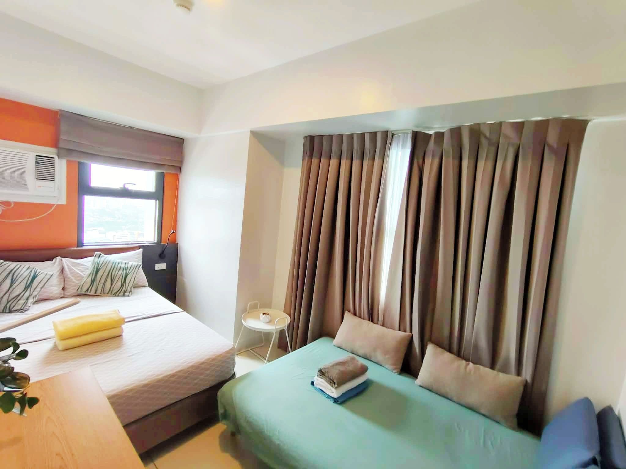 Une chambre d’hôtel avec un lit, une table de chevet, une fenêtre avec des rideaux et un climatiseur fixé au mur.