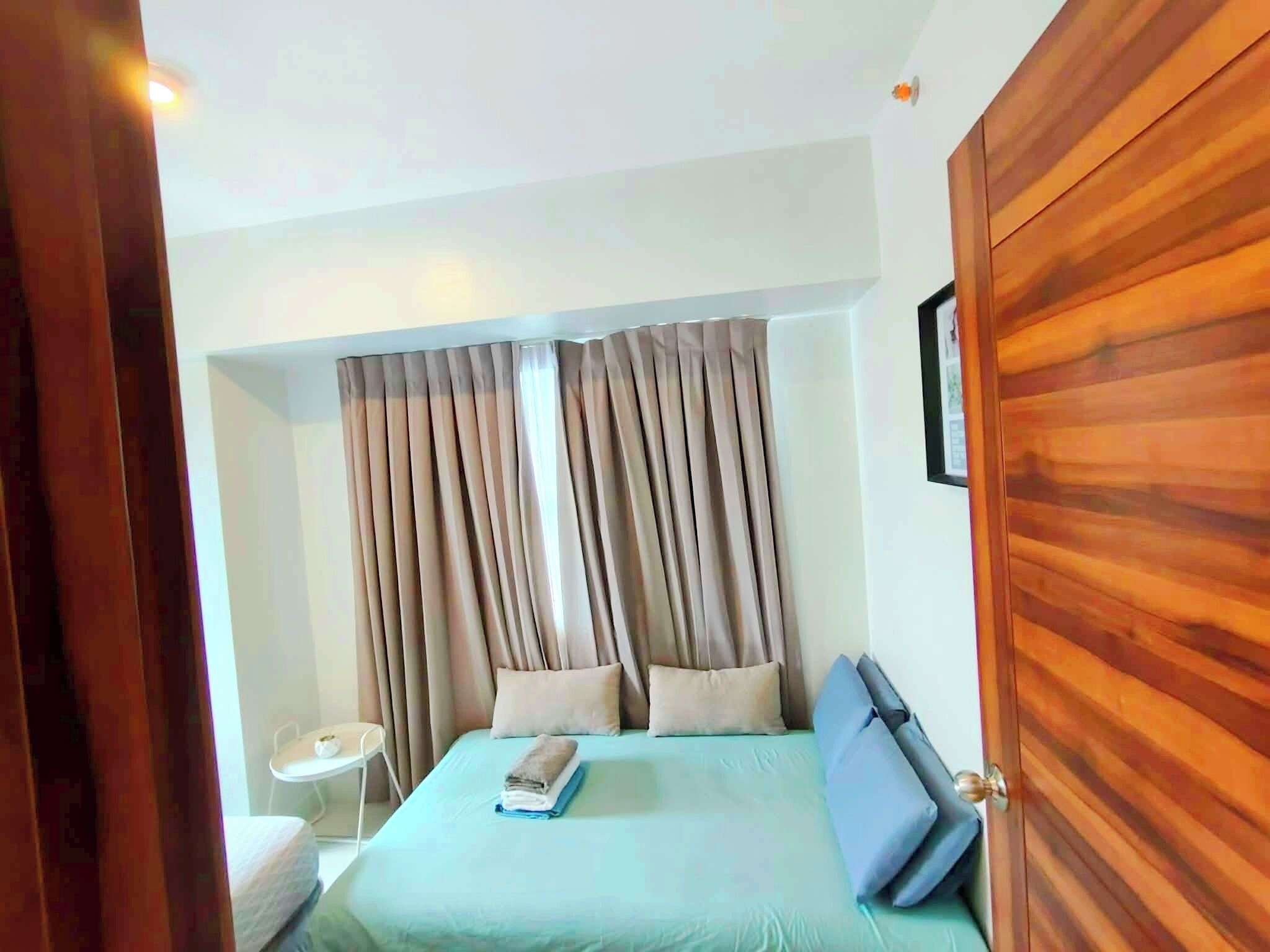 A bedroom with a bed, curtains, a bedside table, and a wooden wardrobe.