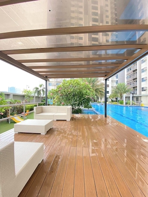 Terraza de madera con mobiliario exterior, piscina y vista a un edificio residencial.