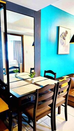 Un comedor con una mesa preparada para cuatro, sillas, una planta en maceta y una pared azul con un cuadro enmarcado.