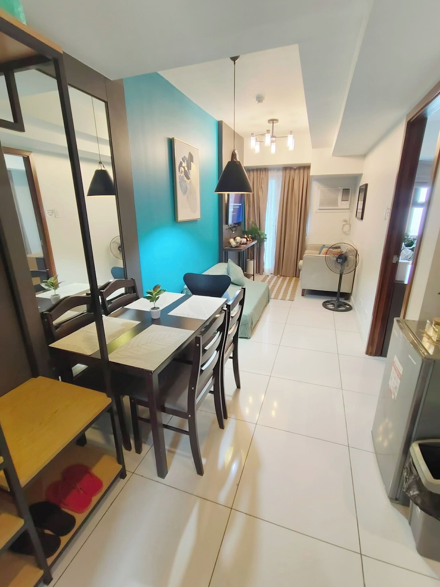 A modern living room with a dining area, a large mirror, a ceiling fan, and a view of the outside.