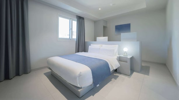 A modern bedroom with a large bed, a bedside table with a lamp, and a window with curtains. - THE M HOTEL (Seoul)