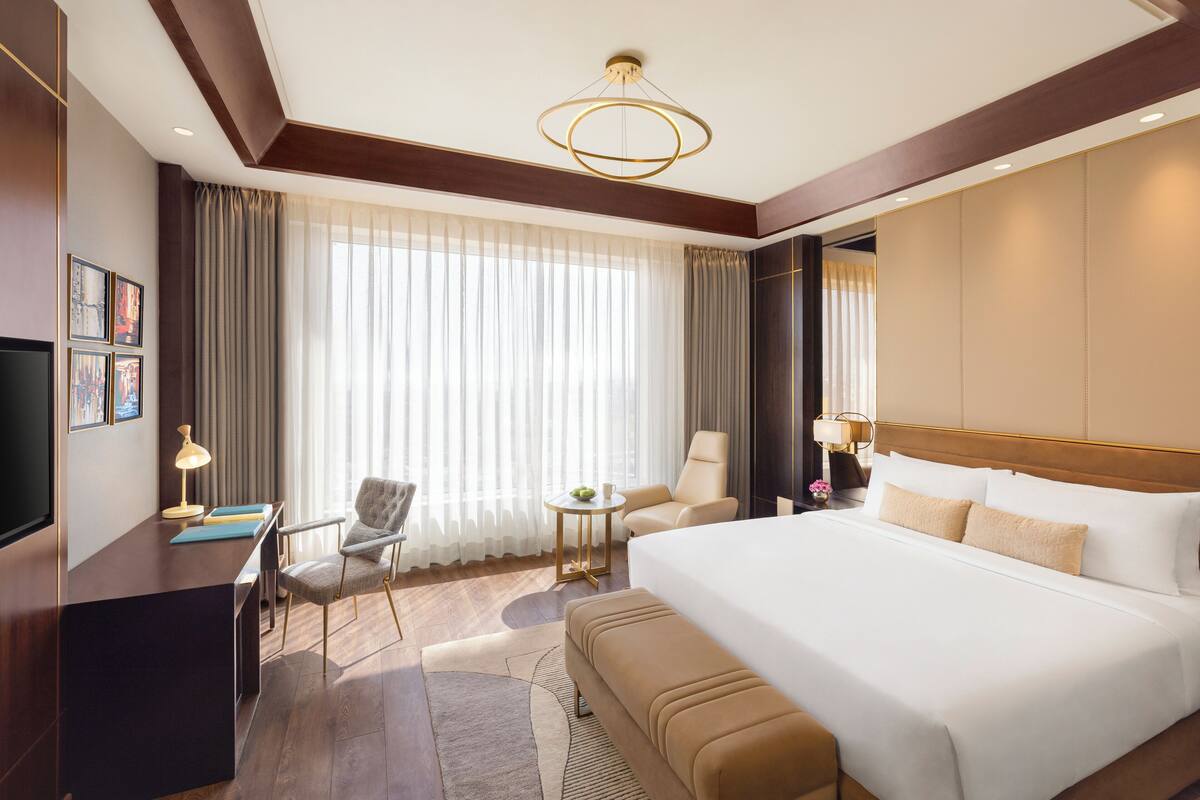 A hotel room with a large bed, a desk, a chair, a TV, and a window with curtains.
