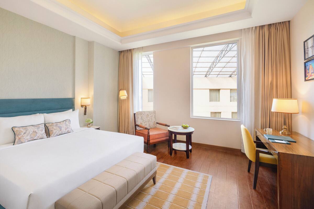 A hotel room with a large bed, a desk, a chair, a small table, and a window with curtains.