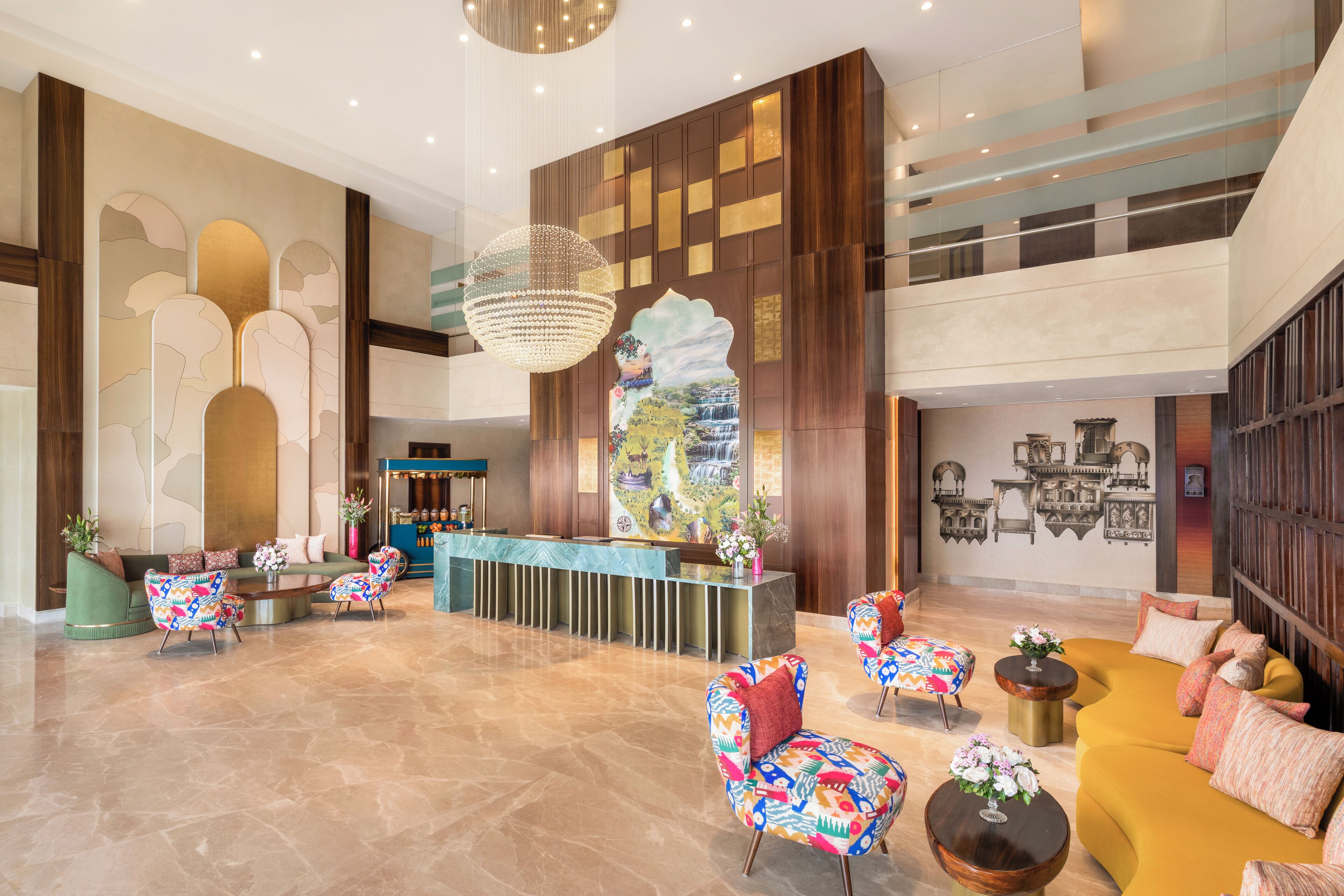 A spacious lobby with a reception desk, colorful patterned chairs, a large chandelier, and a mural on the wall.