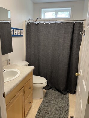 Ein Badezimmer mit weißem Waschbecken, Toilette, Duschvorhang und einer kleinen Fußmatte.