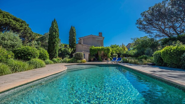 Une piscine à l’eau d’un bleu limpide, entourée de verdure, avec un bâtiment visible au loin.