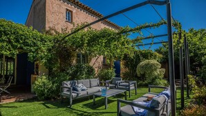 Une terrasse avec des meubles d’extérieur, une pergola et, au fond, un bâtiment doté d’un toit en tuiles.