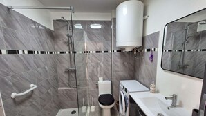 Un bagno moderno con doccia vetro, servizi igienici, lavatrice e lavandino.