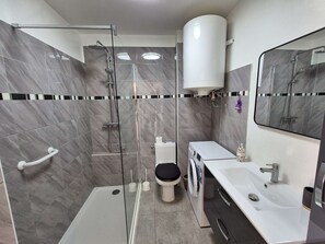 Ein modernes Badezimmer mit Duschkabine, Toilette, Waschmaschine und Waschbecken.