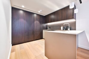 A modern kitchen with dark wood cabinets, a white countertop, and a built-in sink. - Guestready - Stylish Living in Paddington (London)