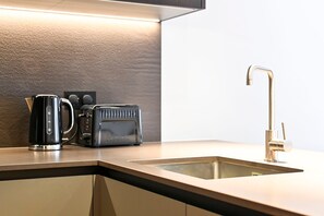 A kitchen with a modern design, featuring a sleek coffee maker, a toaster, and a gold faucet. - Guestready - Stylish Living in Paddington (London)