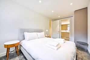 A neatly made bed with white linens, a round wooden side table, and a mirror on the wall. - Guestready - Stylish Living in Paddington (London)