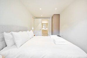 A modern hotel room with a large bed, a bedside table, a lamp, and a view into the bathroom. - Guestready - Stylish Living in Paddington (London)