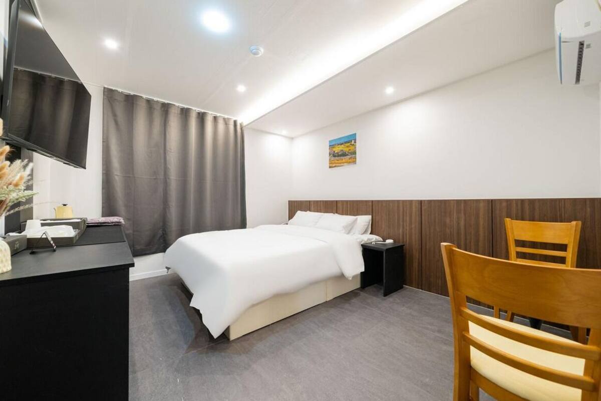 Habitación de hotel con cama, escritorio, silla, televisor y un cuadro en la pared.