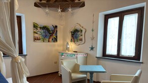 Una habitación acogedora con una silla blanca, una mesita y un ventanal con cortinas. Hay dos cuadros en la pared y una estrella decorativa colgando.