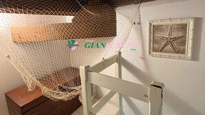Una habitación con una silla de madera, una pared blanca con un cuadro de una estrella de mar, y una red colgada del techo.