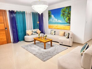 Een woonkamer met een beige bank, een houten salontafel en een schilderij van een zandstrand.