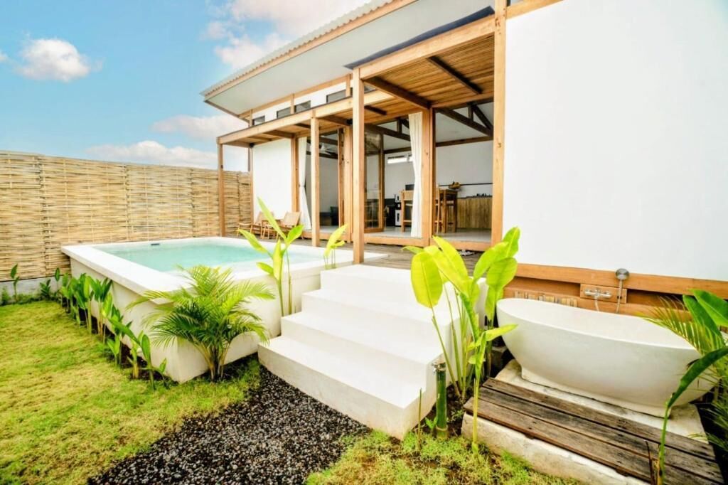 Un área de piscina moderna al aire libre con un jacuzzi, escalones que conducen a un porche cubierto y abundante vegetación.