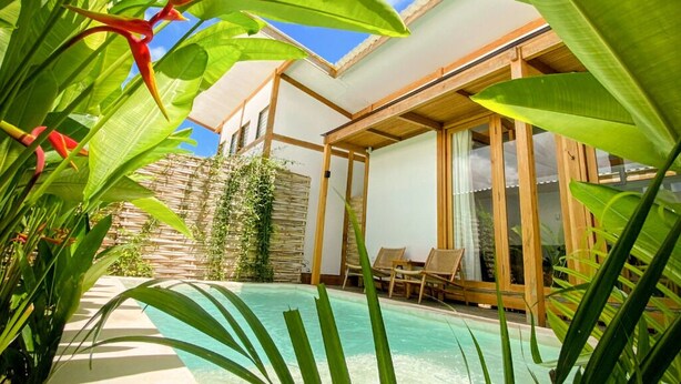 Une maison moderne avec une piscine, entourée d’une végétation luxuriante et sous un ciel dégagé.