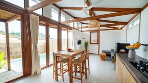 Une cuisine spacieuse avec des poutres en bois, une table à manger avec des chaises, une grande fenêtre et une vue sur une piscine.