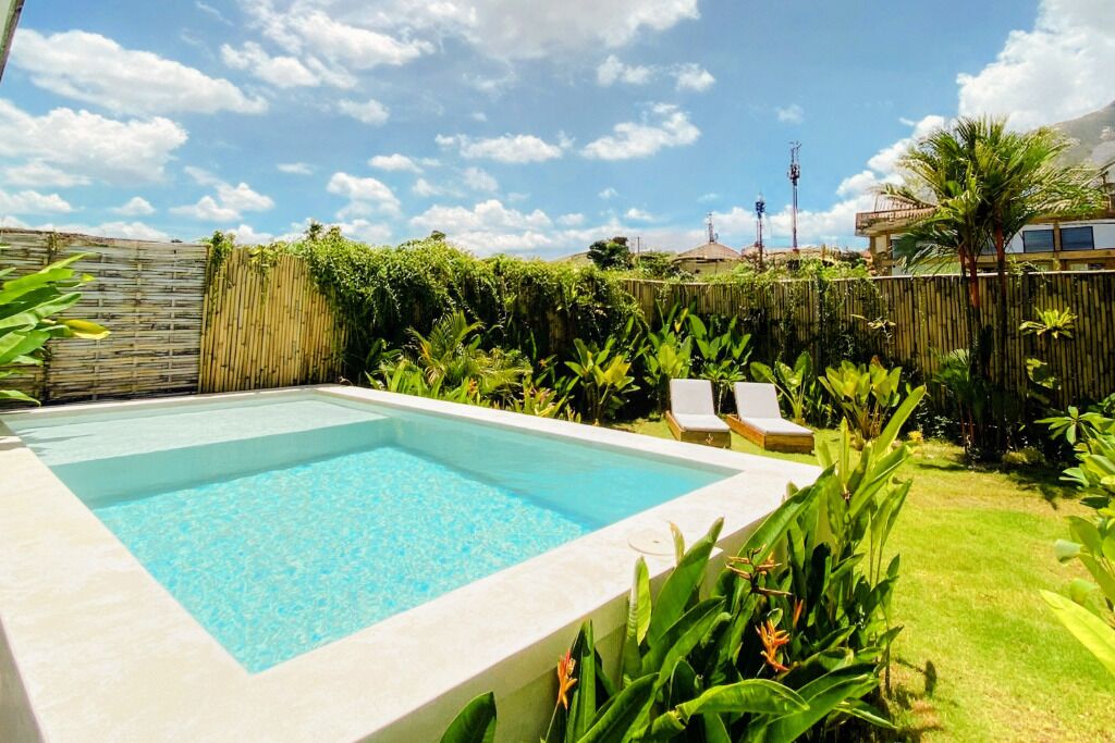 A rectangular swimming pool with clear blue water, surrounded by lush greenery and a bamboo fence.