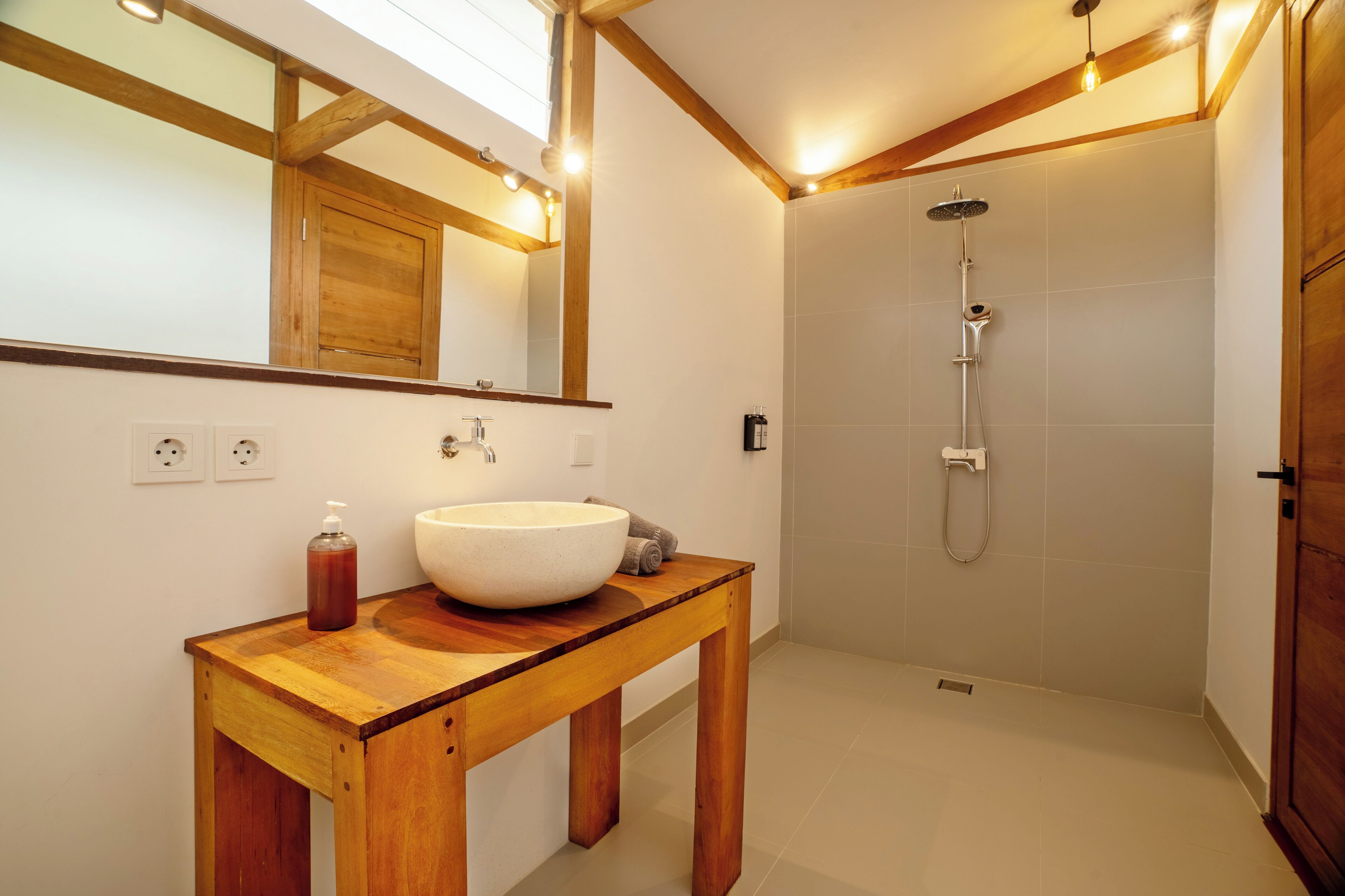 Un baño con tocador de madera, un espejo grande, un lavamanos blanco y una zona de ducha.