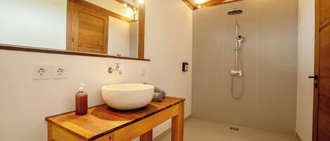Un baño con tocador de madera, un espejo grande, un lavamanos blanco y una zona de ducha.