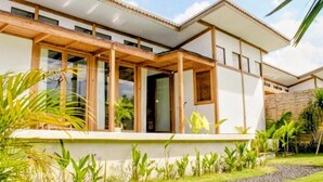 Une maison moderne dotée d’une terrasse en bois, de grandes fenêtres et d’un jardin bien entretenu.