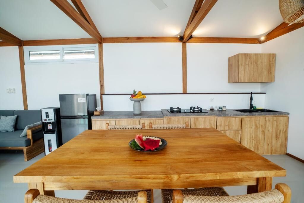 A modern kitchen with wooden beams, a dining table with a fruit bowl, and a grey sofa.