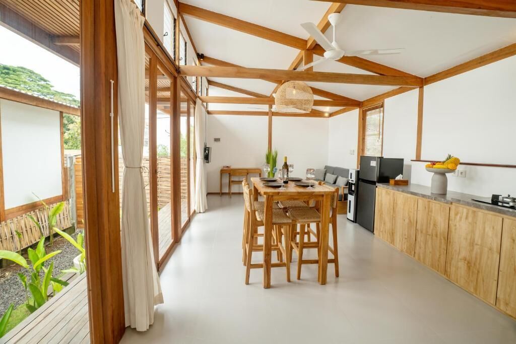 Eine moderne Küche mit Holzbalken, einem Essbereich mit Tisch und Stühlen sowie Blick ins Freie.