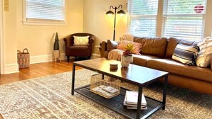 Un salon avec un canapé en cuir marron, une table basse en bois, un tapis à motifs et une plante décorative.