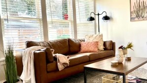 Un salon avec un canapé en cuir marron, une table basse et une grande fenêtre équipée de stores.