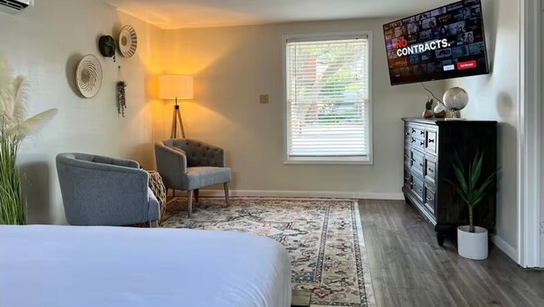 Une chambre à coucher comprenant un lit, une chaise, une commode, un téléviseur et une fenêtre avec des stores.