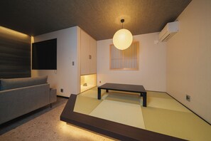 A room with tatami flooring, a low table, a sofa, a wall-mounted air conditioner, and a hanging light fixture. - GAON (Beppu)