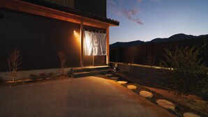 A modern house with a wooden exterior, a well-lit entrance, and a view of mountains in the background. - GAON (Beppu)