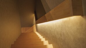 A wooden staircase with a textured wall on one side and a smooth wall on the other, leading to a higher floor. - GAON (Beppu)