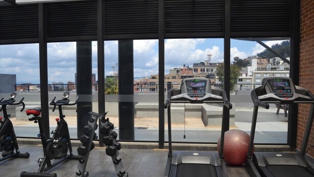 Una palestra con attrezzature per esercizi, tra cui tapis roulant e cyclette, e un'ampia finestra che offre vista sulla città.