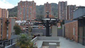 Una terrazza sul tetto con una scultura moderna, circondata da edifici residenziali e uno sfondo collinare.