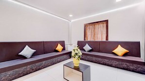 A modern lobby with two dark brown sofas, a central coffee table with a vase of flowers, and a large window with a curtain. - Collection O Ramanathapuram (Ramanathapuram)