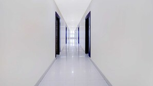 A long, narrow hallway with white walls and a shiny tiled floor, leading to a bright area at the end. - Collection O Ramanathapuram (Ramanathapuram)