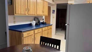 Een compacte keuken met houten kastjes, een blauw aanrecht, een koffiezetapparaat en een koelkast.