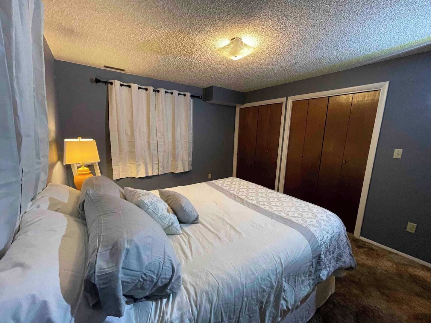 A bedroom with a bed, curtains, a nightstand, and a wardrobe.