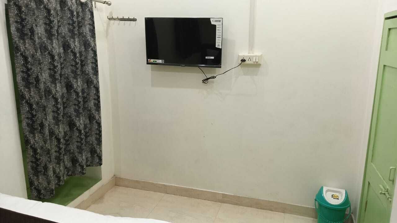 A small room with a television mounted on the wall, a green bucket, and a green door.