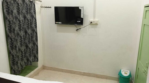 Une petite pièce avec un téléviseur fixé au mur, un seau vert et une porte verte.