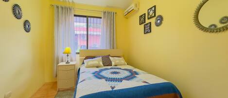 A bedroom with a bed, a nightstand, a lamp, a window with curtains, and wall decorations.
