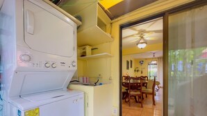 Un área de lavandería con lavadora y secadora de carga frontal, un comedor con mesa y sillas, y un ventilador de techo.