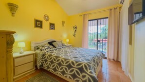Un dormitorio con cama, mesitas de noche, lámpara, ventilador de techo y ventana con cortinas.